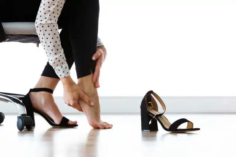 Woman taking off painful high heel shoe and comforting her feet
