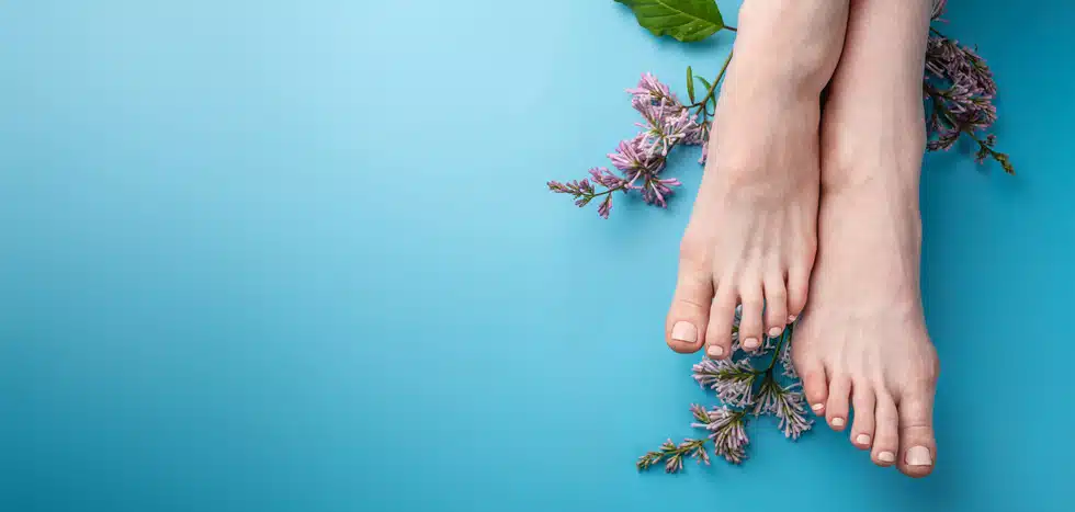 female feet laying on top of flowers in front of blue background