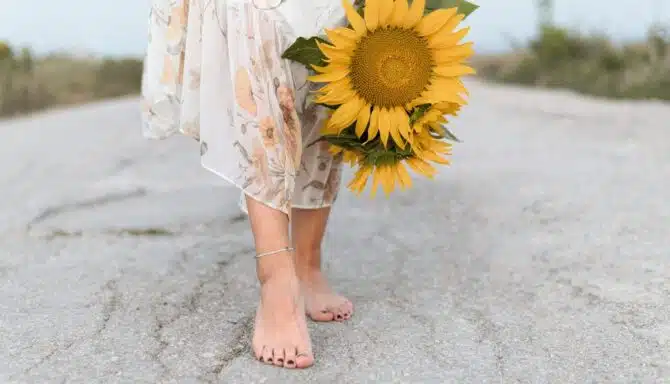 Woman's lower legs and feet holding bunch of large yellow sunflowers