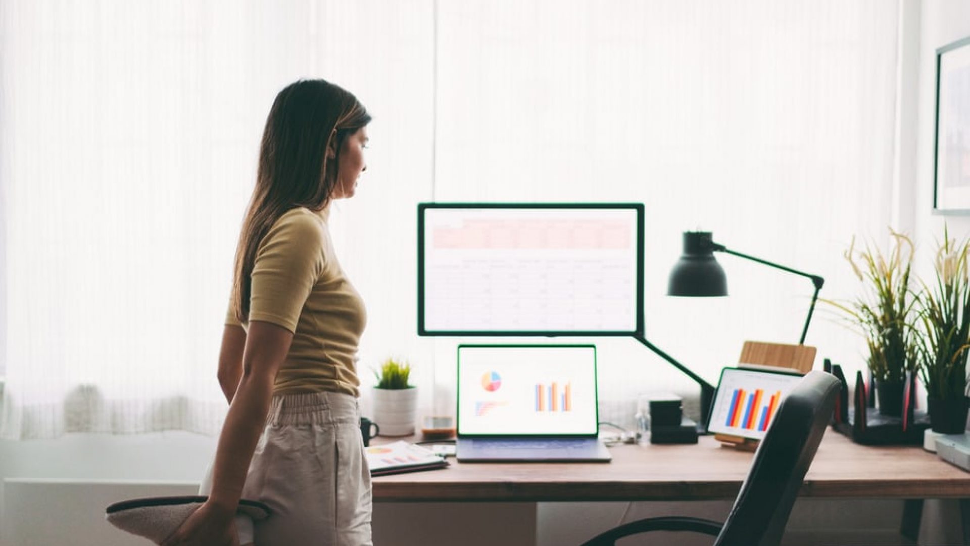 Woman stretching foot while standing in front of desktop computer