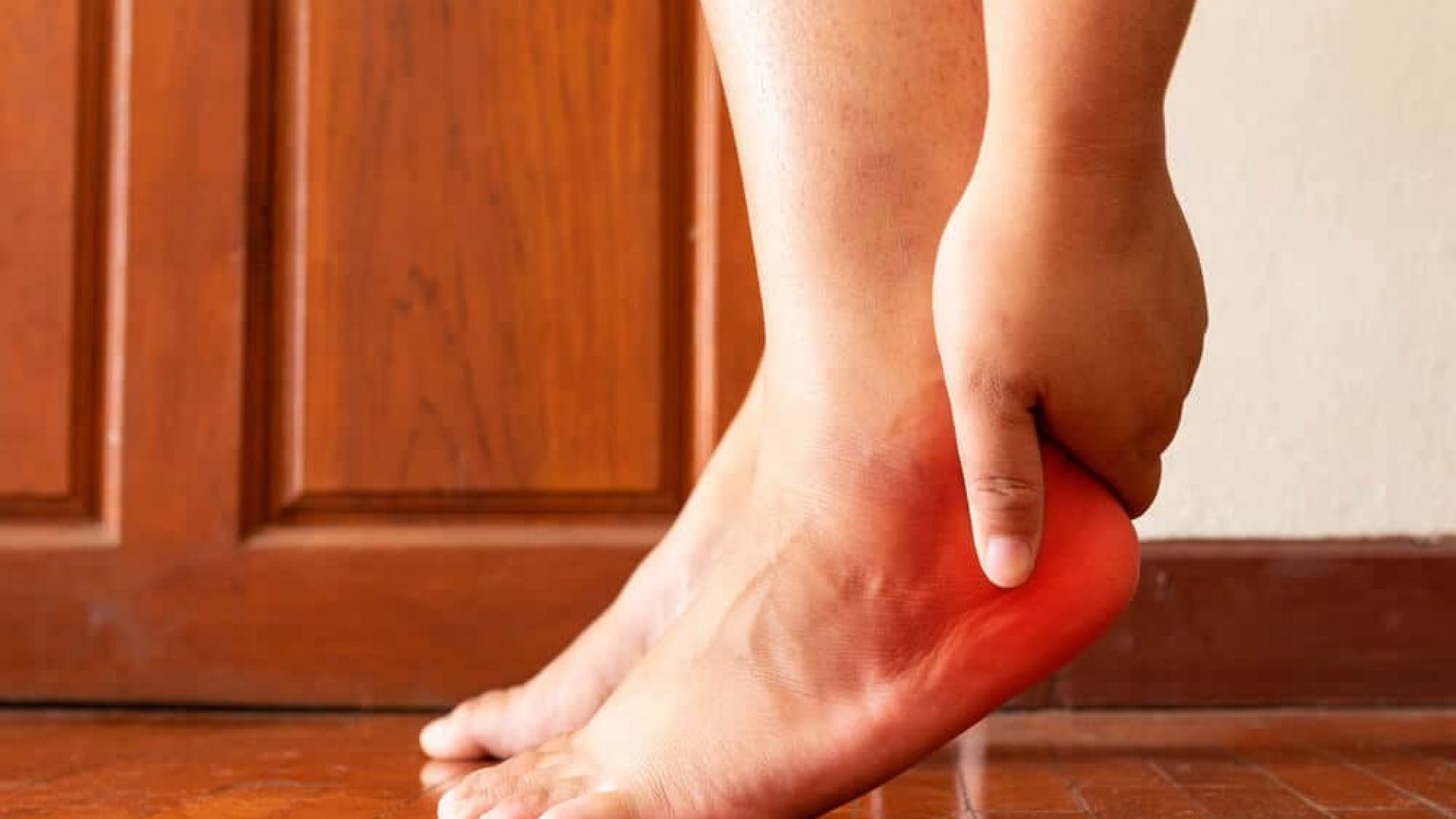 Person elevating flat foot slightly using toes and holding their heel experiencing plantar fasciitis pain