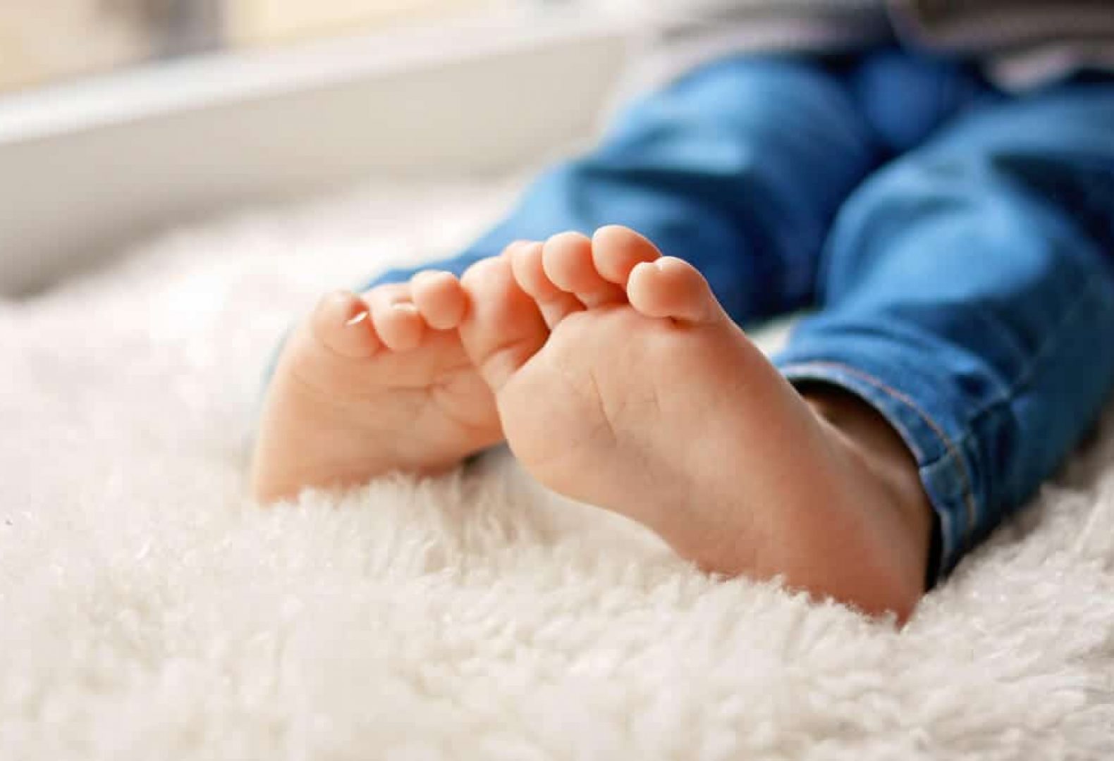 close up of child's feet on white rug wearing blue pant or jeans