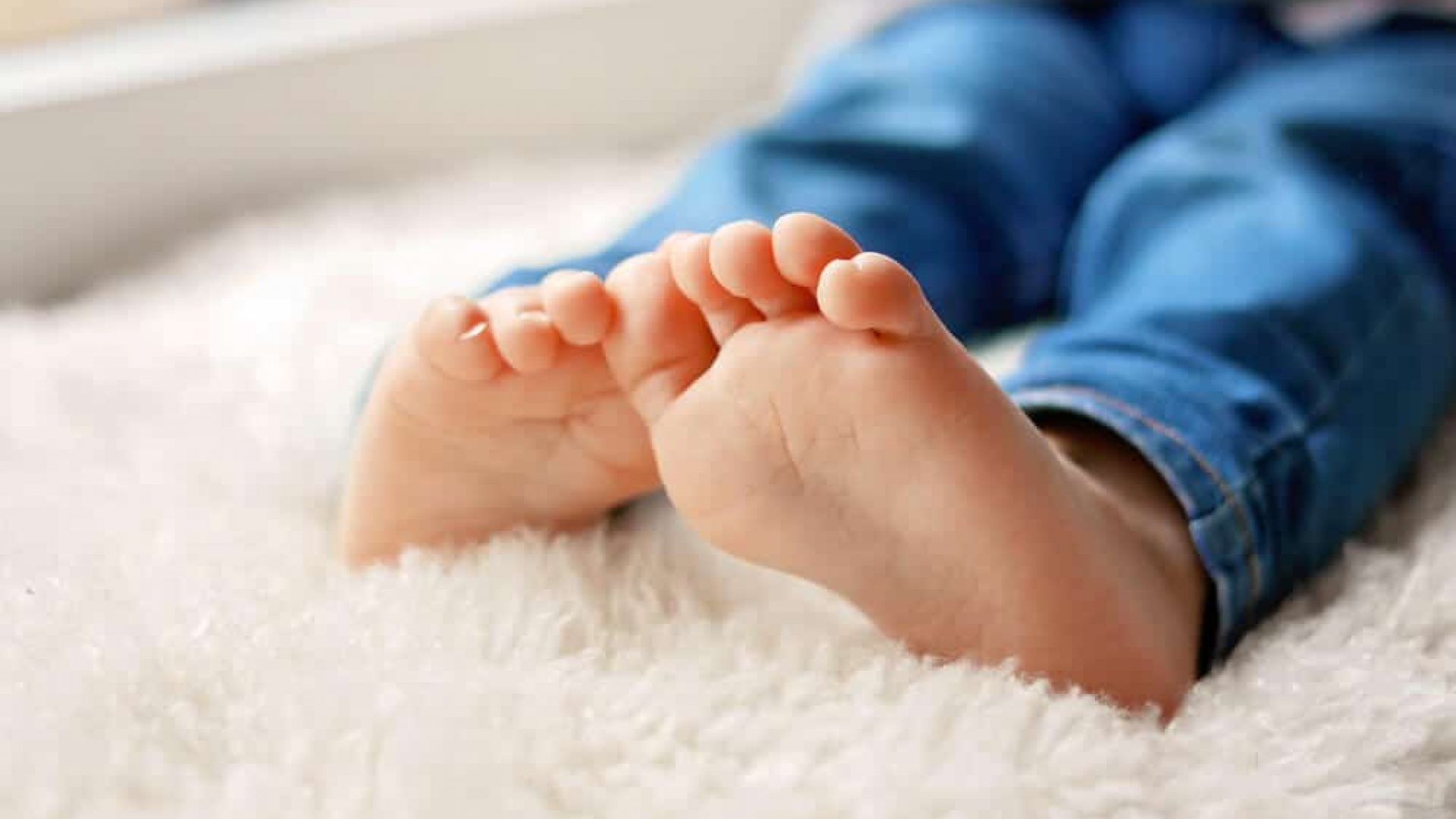 close up of child's feet on white rug wearing blue pant or jeans