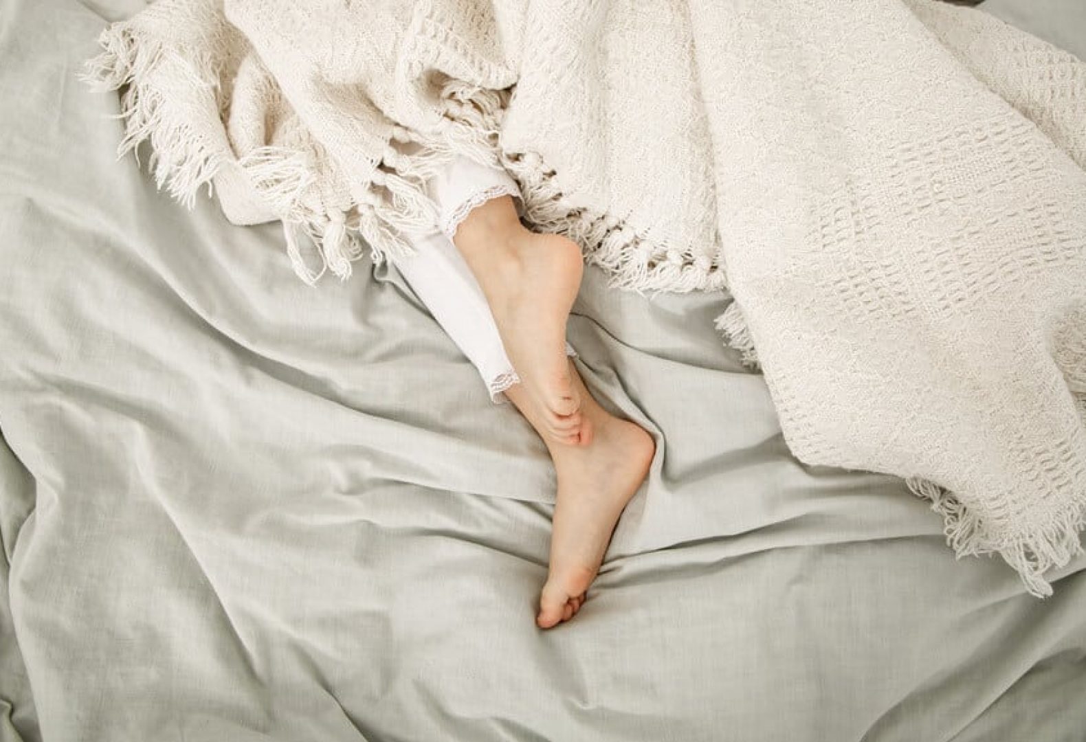 female feet underneath off white blankets on top of off white sheets