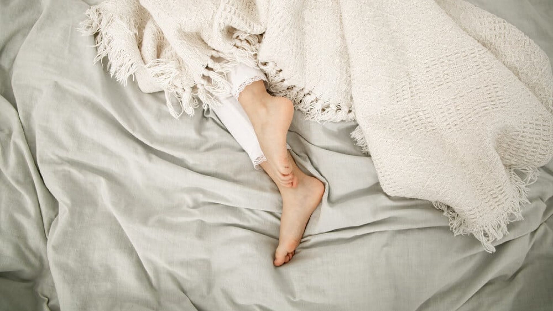 female feet underneath off white blankets on top of off white sheets