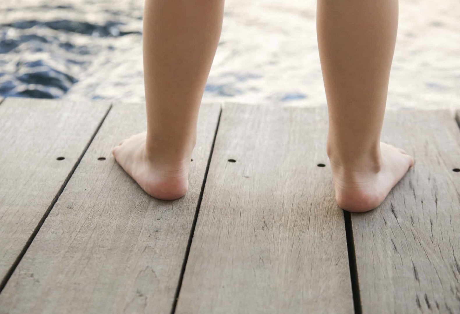 A child with flat feet standing on wooden platform next to the water