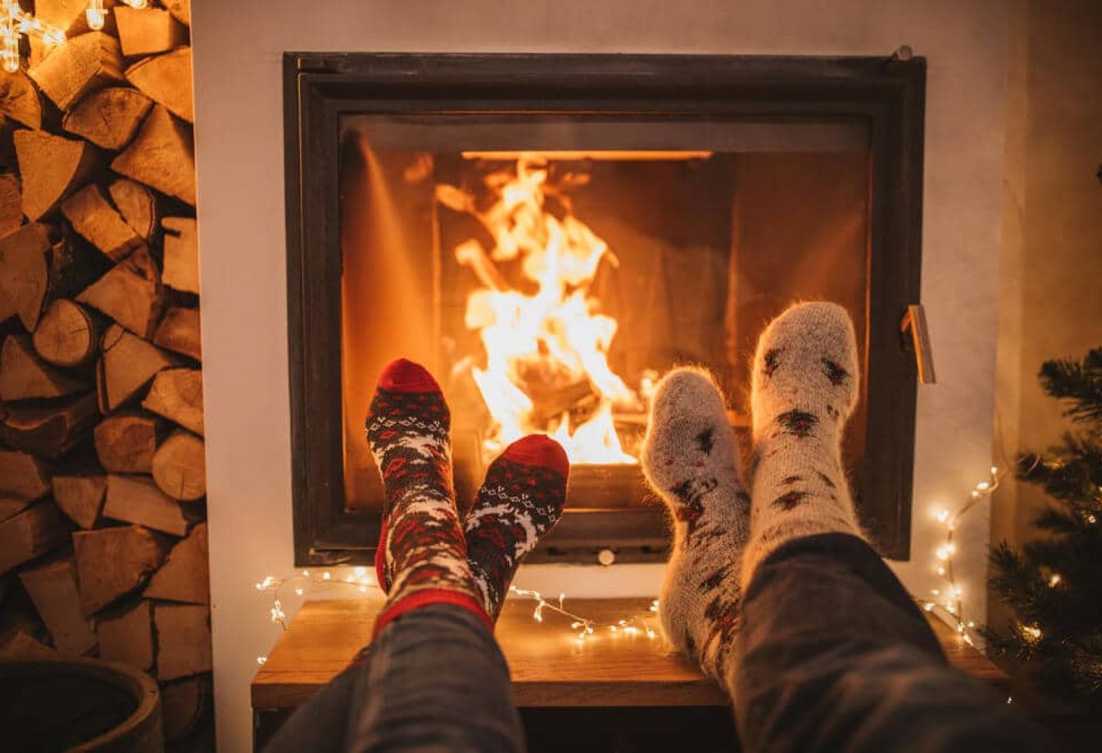 cozy fireplace dimly lit with two pairs of feet next to it wearing wool socks