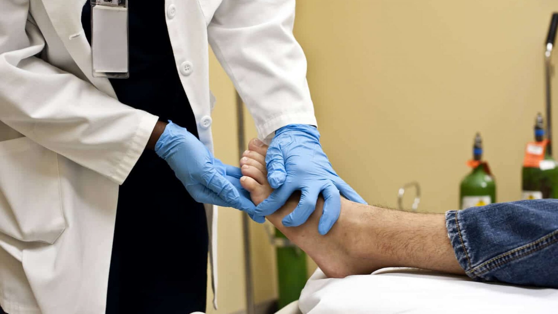 foot specialist like a chiropodist or podiatrist wearing blue globes and tending to a male patient