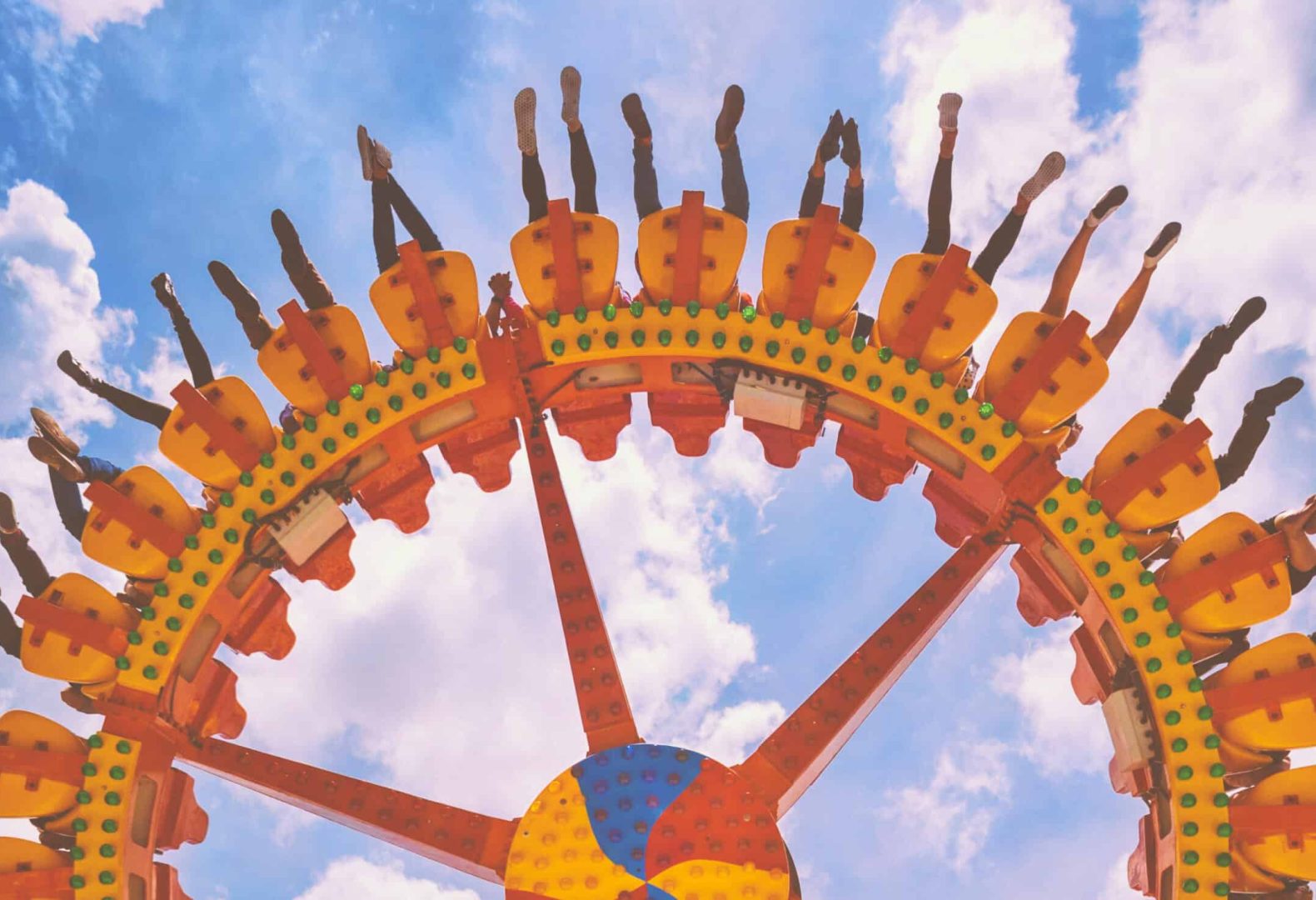 Funny photo of legs of women, men in amusement park riding with fun on extreme attraction swinging upside down high in air on sky background. Family lifestyle, people activity on holiday with children