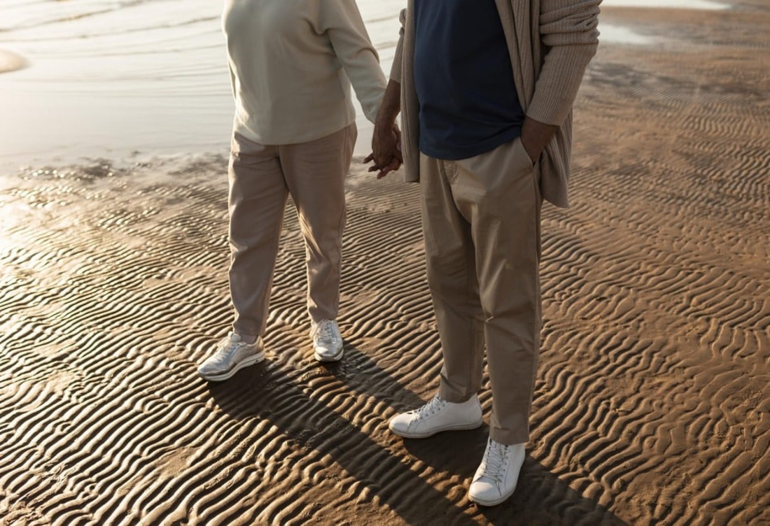 Male and female senior with casual lounge clothes and white sneakers on the beach holding hands