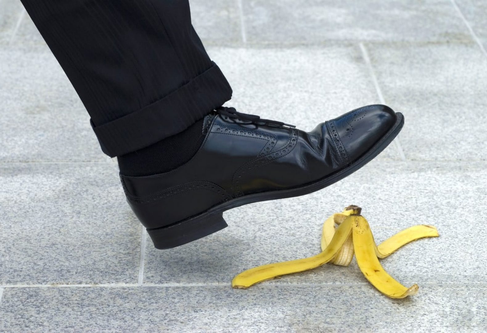 Dress shoe on tiled walkway about to slip on a banana peel