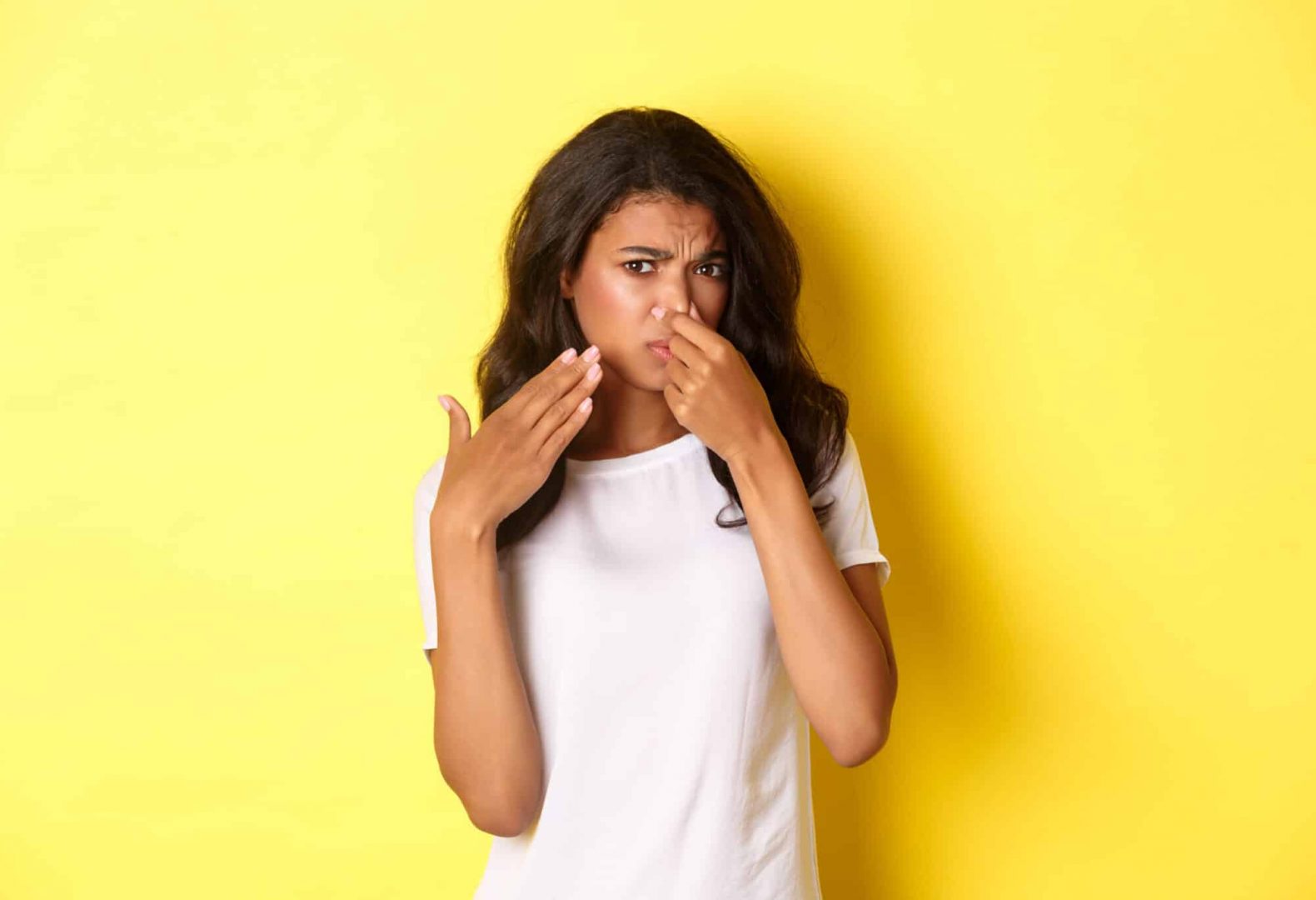 Portrait of young african-american girl, shut her nose and looking at something with disgusting smell, complaining on bad stink, standing over yellow background.