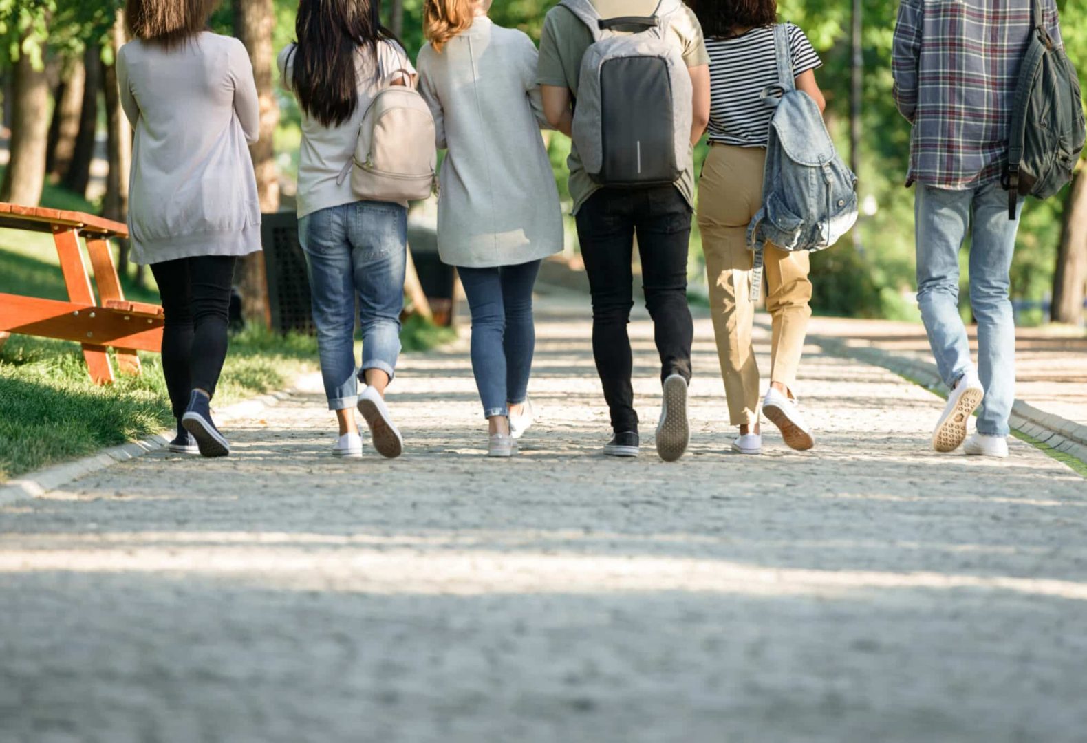 Back view cropped picture of multiethnic group of young students walking outdoors.