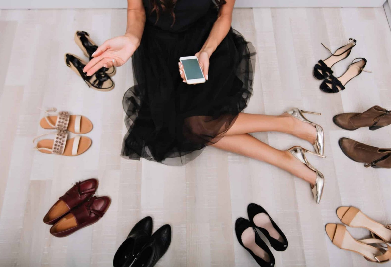 Woman sitting on the floor in the middle of several pairs of high heel shoes