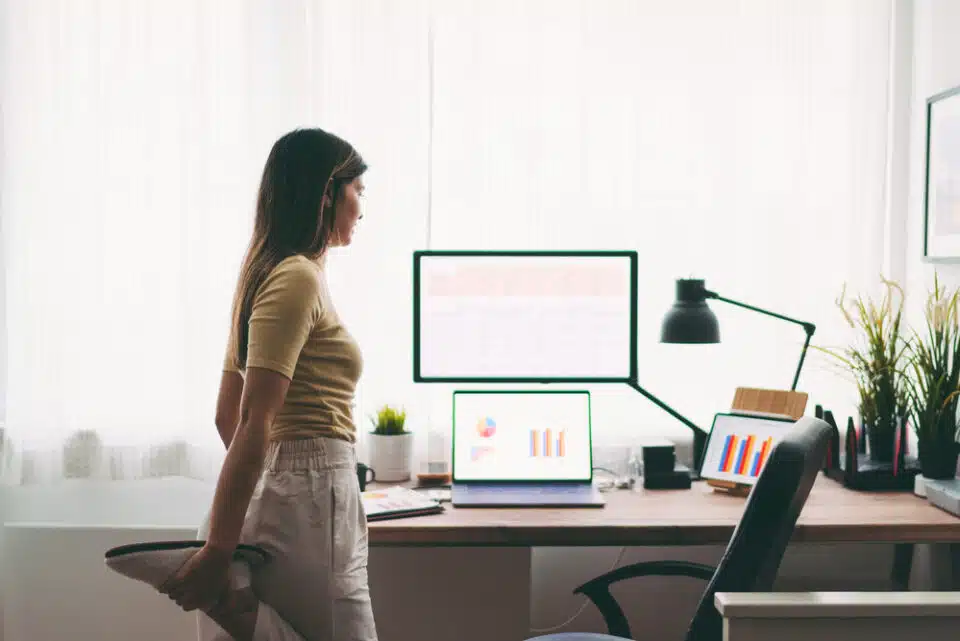 Woman stretching foot while standing in front of desktop computer