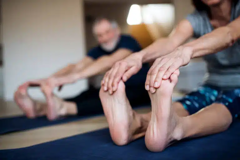 two older adults performing foot stretches close up on the bottom of the foot, pulling toes towards them