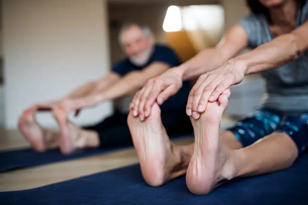 Two older adults one man and one woman performing foot stretching exercises on the floor