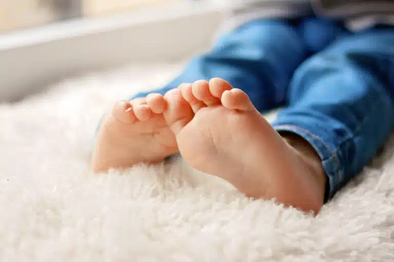 close up of child's feet on white rug wearing blue pant or jeans