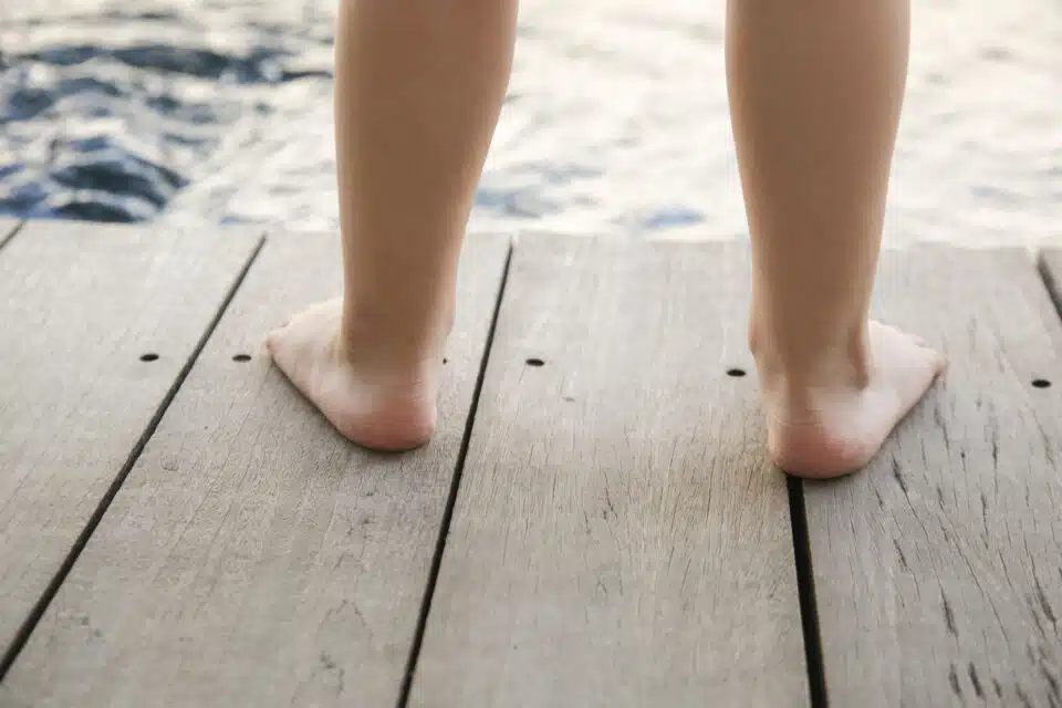 A child with flat feet standing on wooden platform next to the water