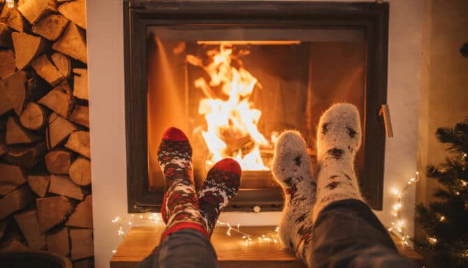 cozy fireplace dimly lit with two pairs of feet next to it wearing wool socks