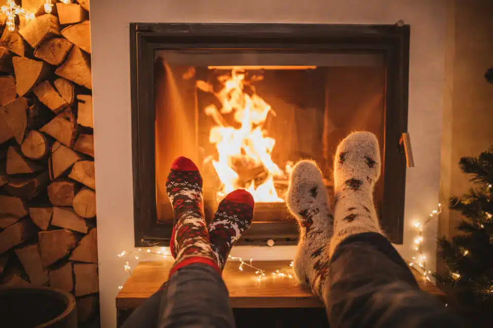 cozy fireplace dimly lit with two pairs of feet next to it wearing wool socks