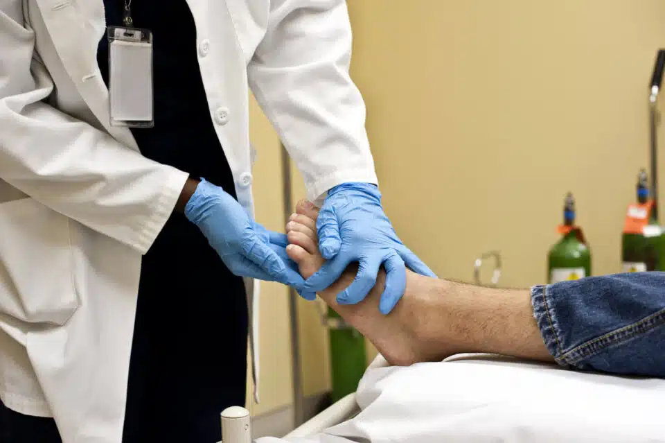 foot specialist like a chiropodist or podiatrist wearing blue globes and tending to a male patient