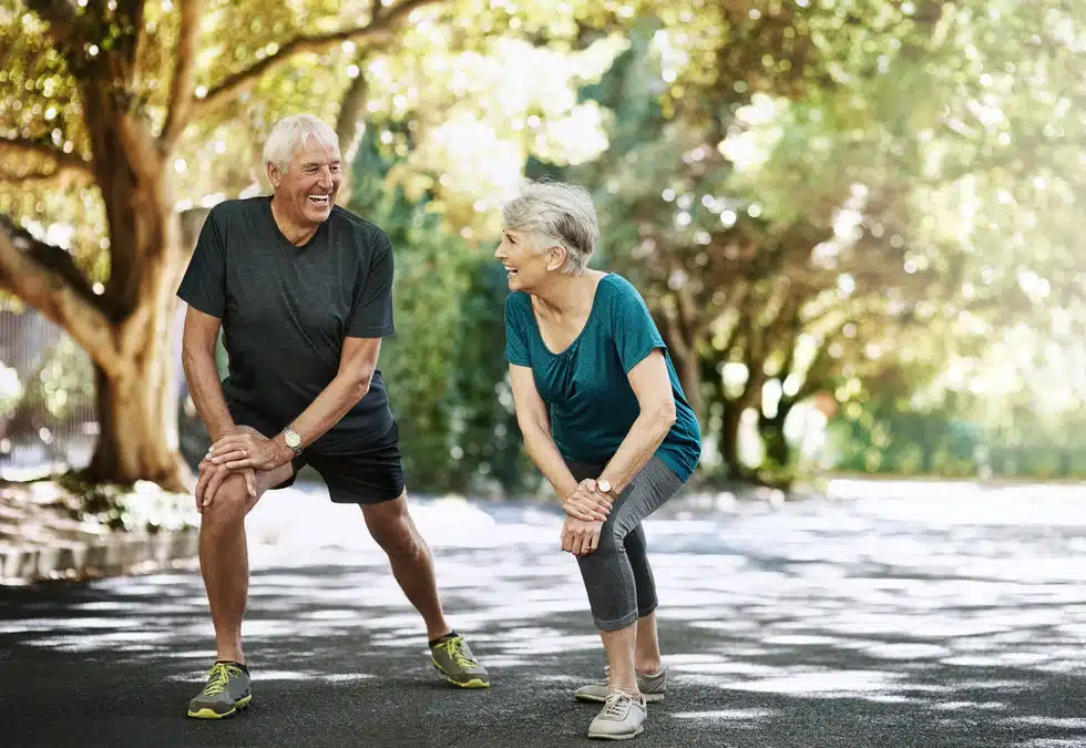 Male and female senior smiling at each other as they both stretch their knees preparing for exercise