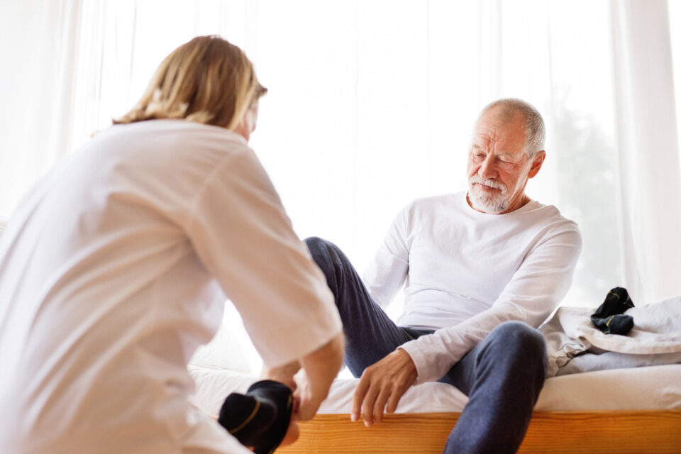 Man visiting doctor or specialist about a foot concern, female specialist lifting his foot up for him