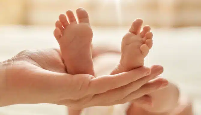 Mother's hand holding newborn baby's barefoot, mommy making massage for infant for normalization of the nervous system and development of coordination of movements.