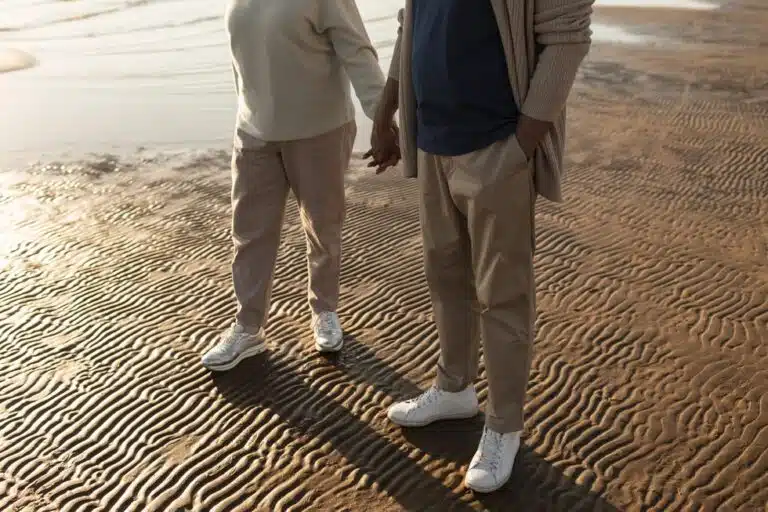 Male and female senior with casual lounge clothes and white sneakers on the beach holding hands