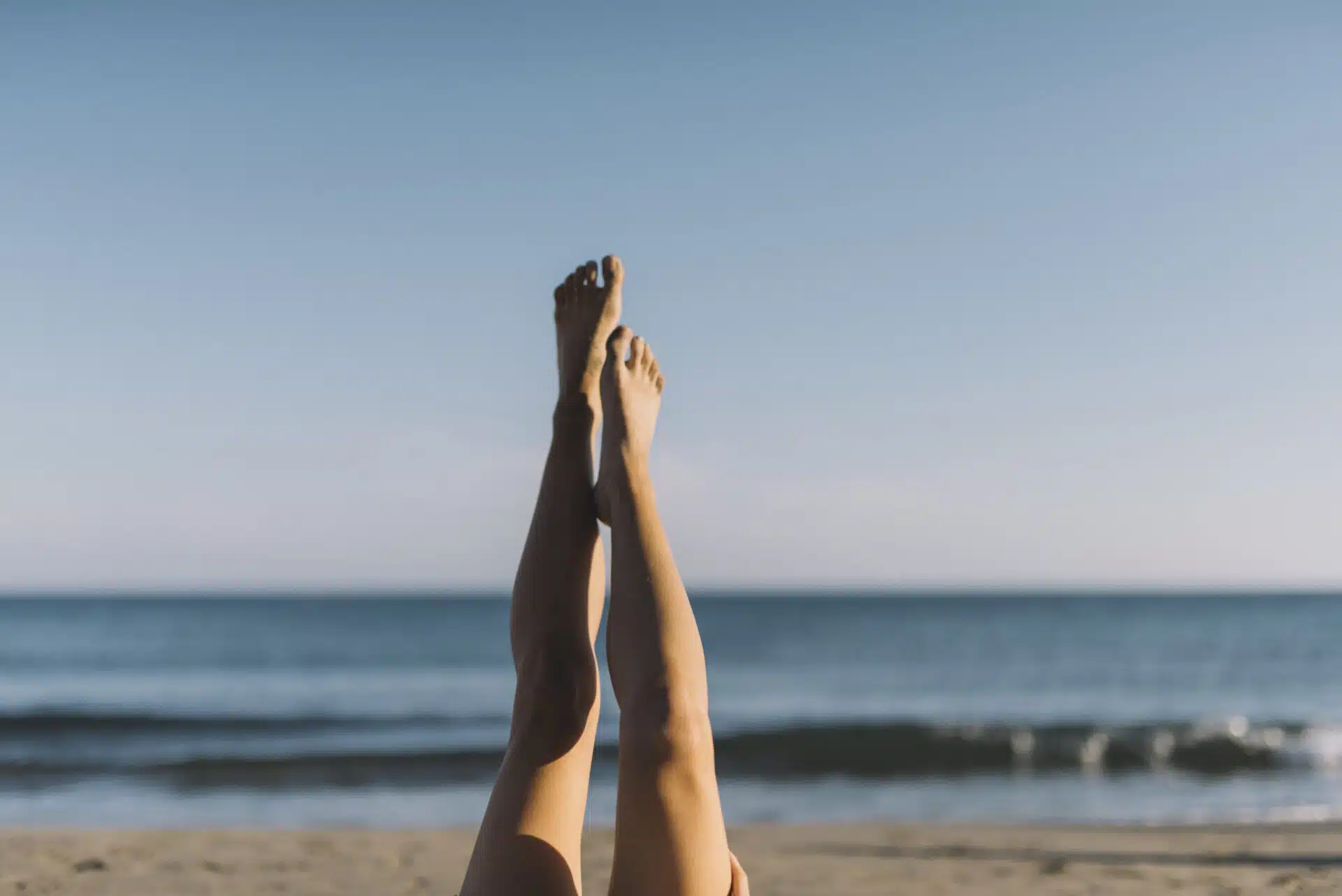 Woman enjoying sun on the beach lifting legs in the air